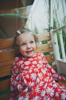 girl in red and white floral dress sitting on brown wooden bench