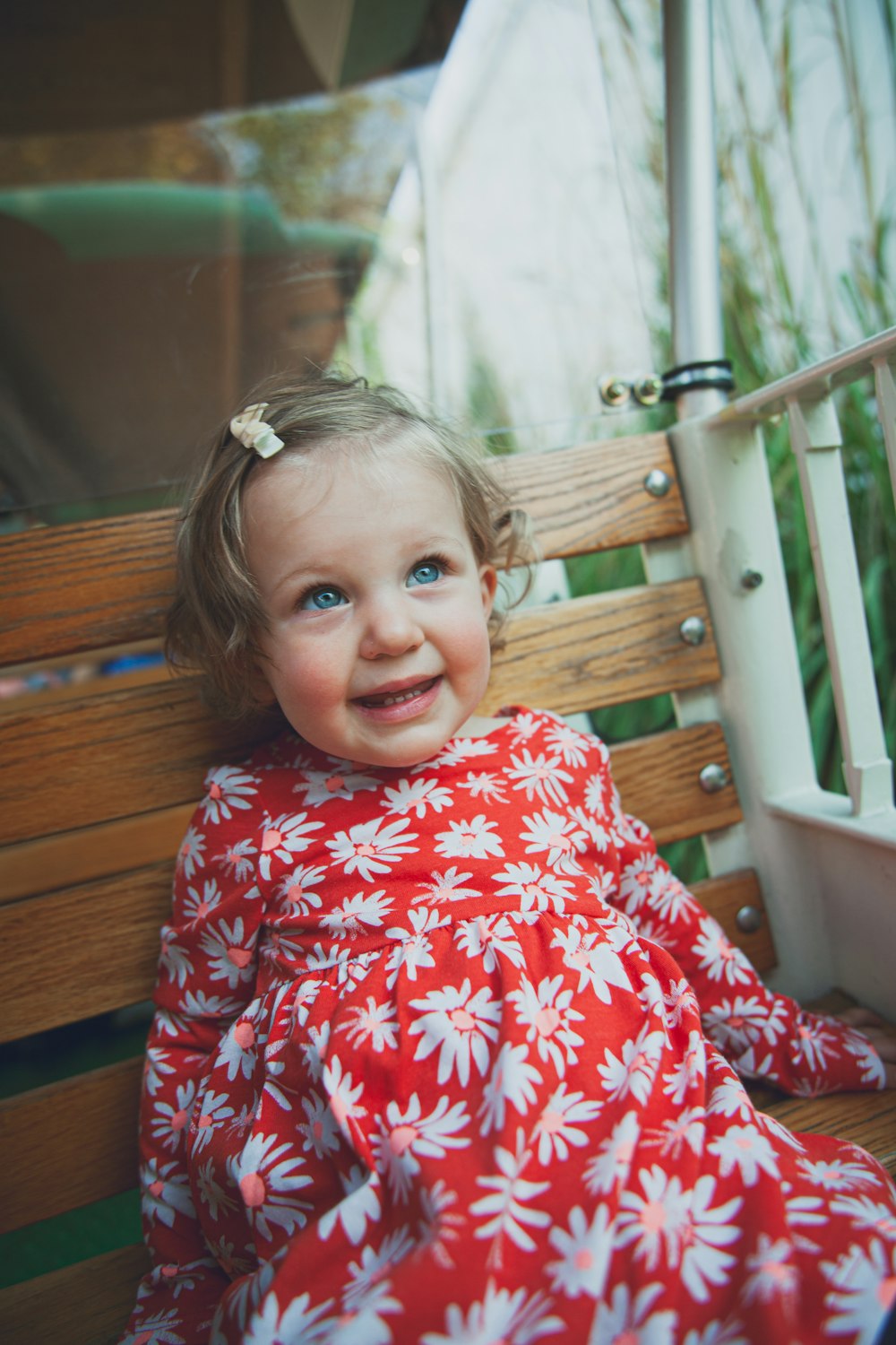 girl in red and white floral dress sitting on brown wooden bench