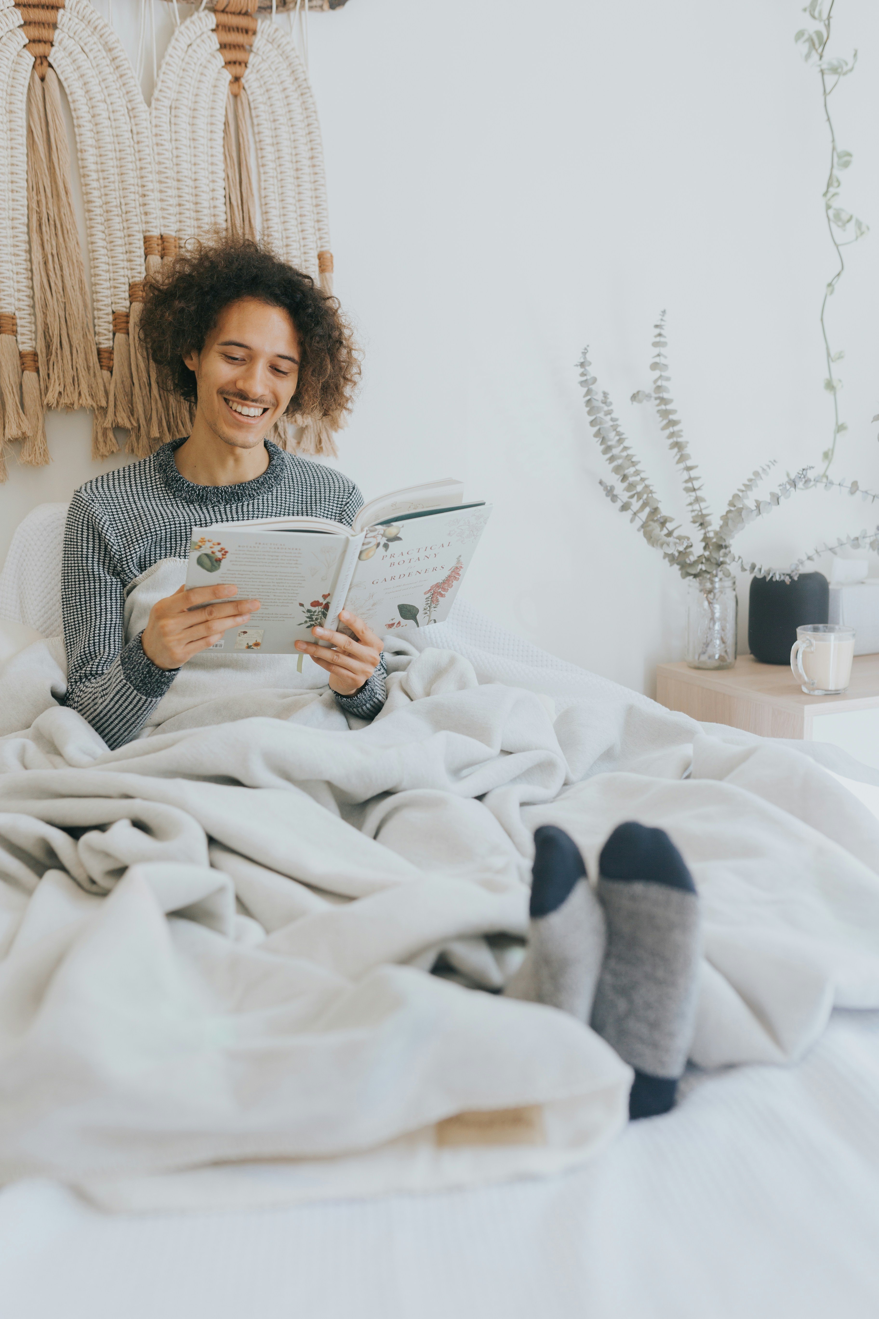 Person reads a book in bed, wrapped in a blanket.