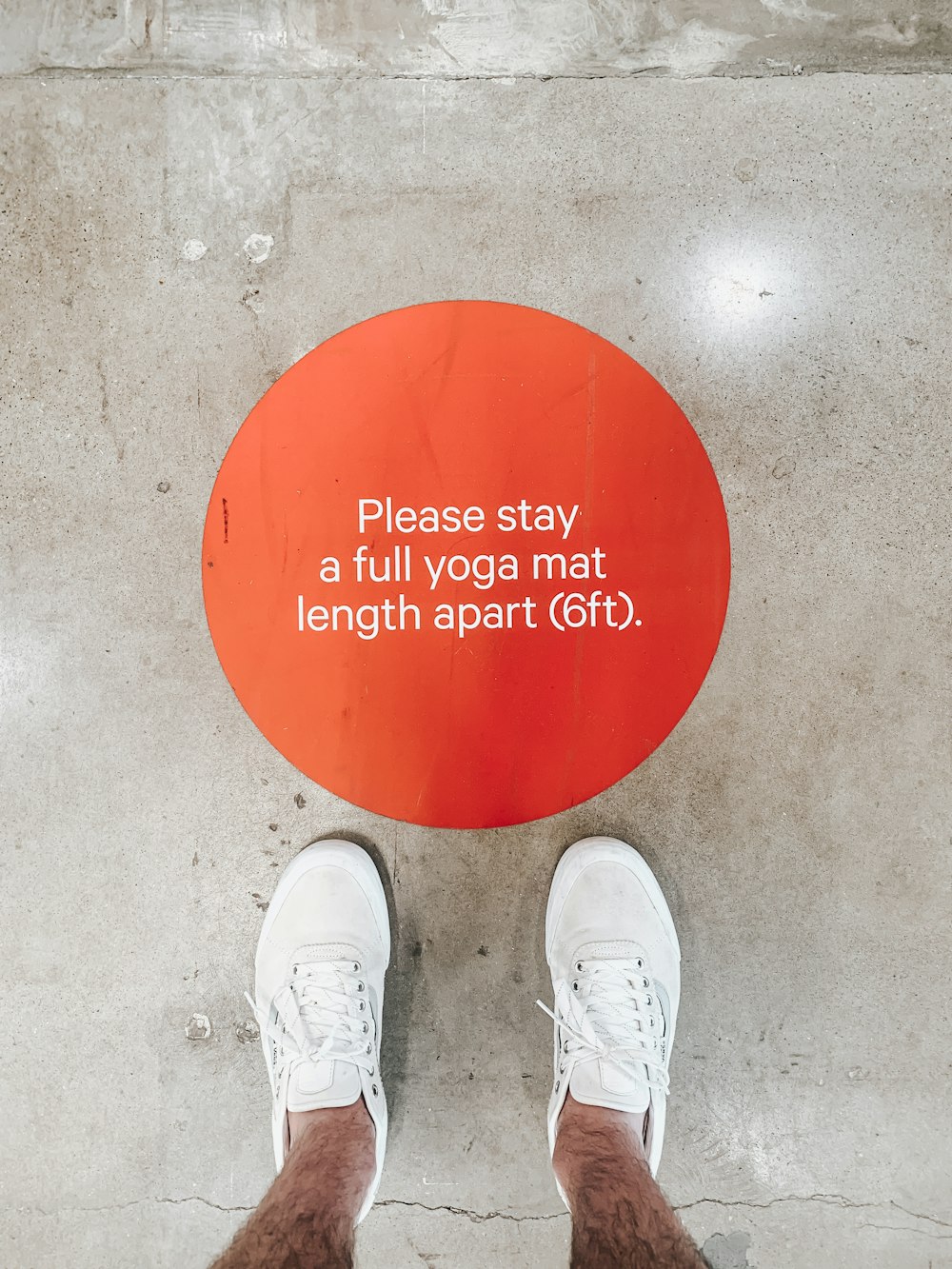 person in white sneakers standing on red round floor mat