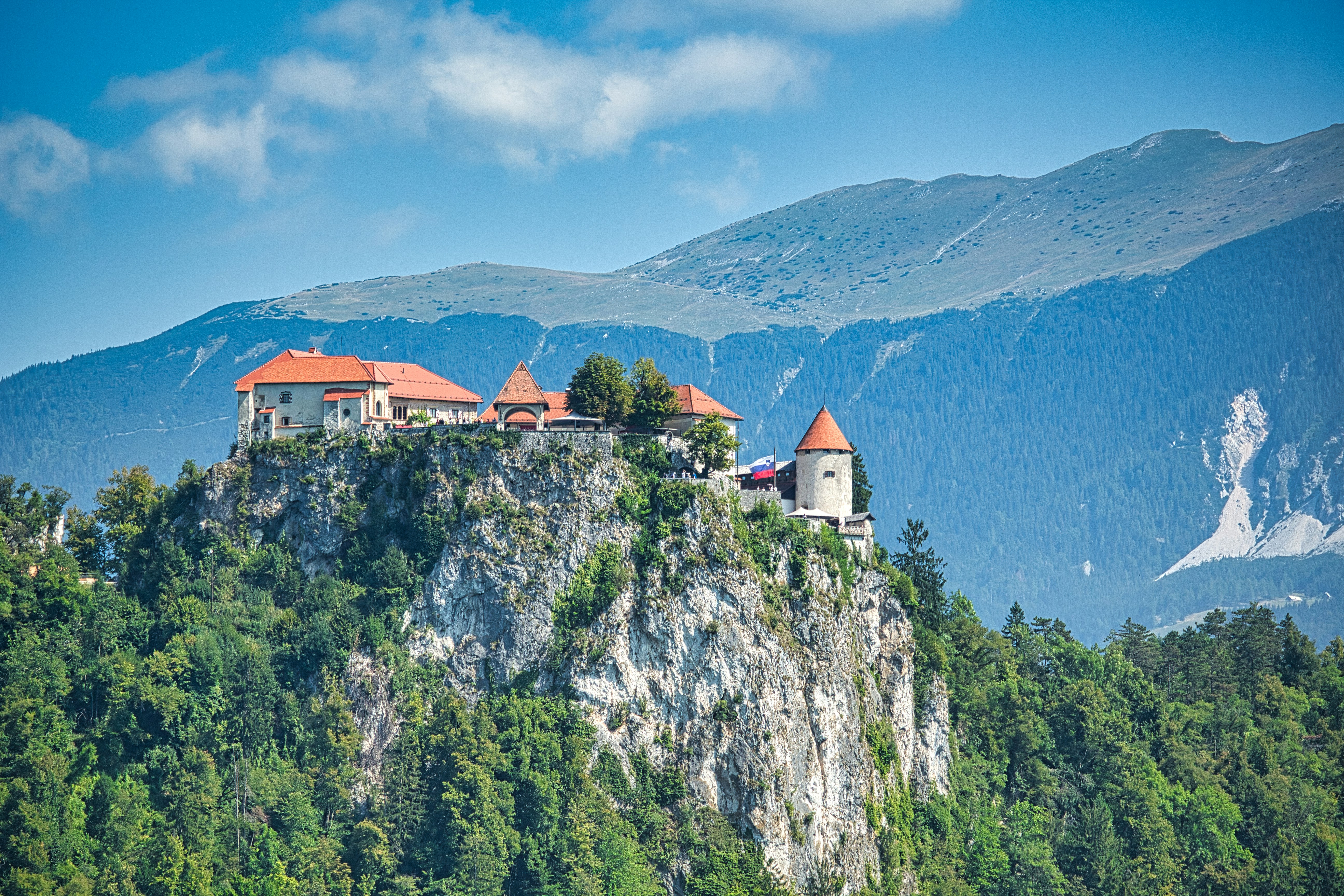 white and brown house on top of mountain during daytime, An old castle built on the edge of a cliff over Lake Bled