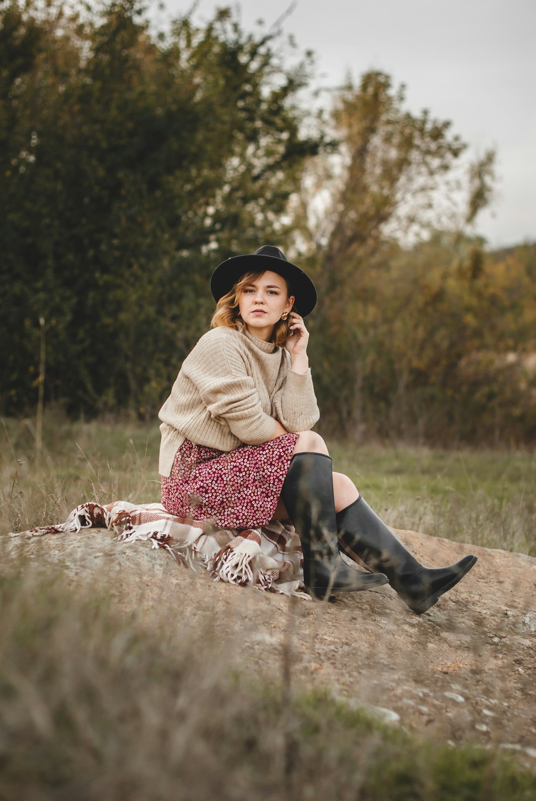 woman in beige sweater and black and white skirt sitting on brown grass field during daytime