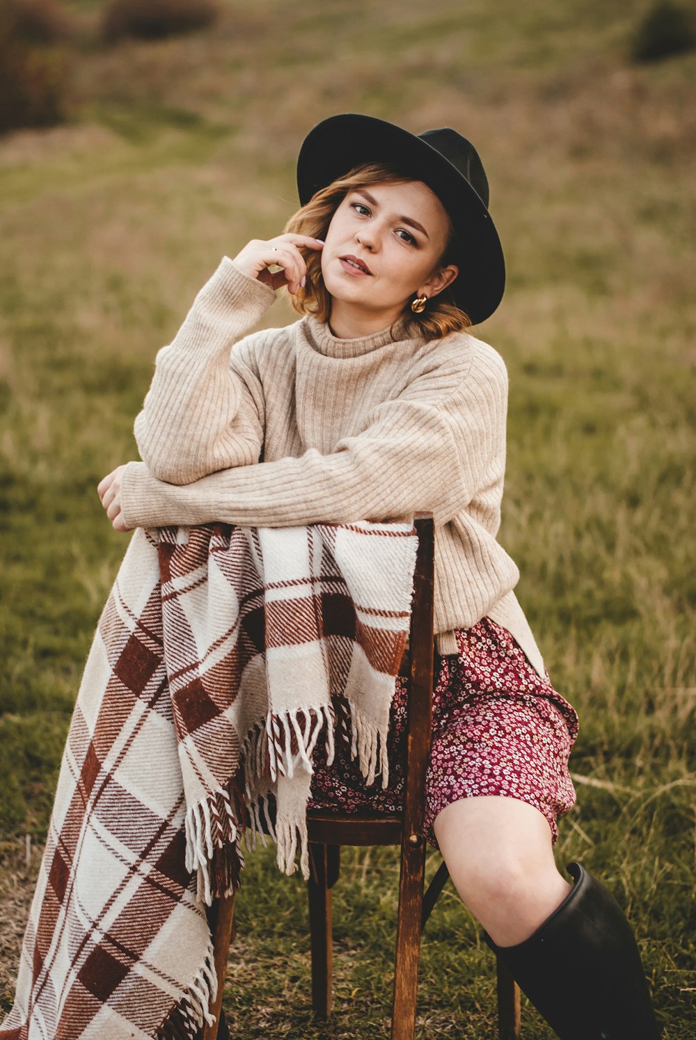 woman in white sweater and black and white plaid skirt sitting on green grass field during