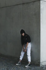 Dark, minimalist urban scene with a model wearing edgy streetwear against a concrete wall.