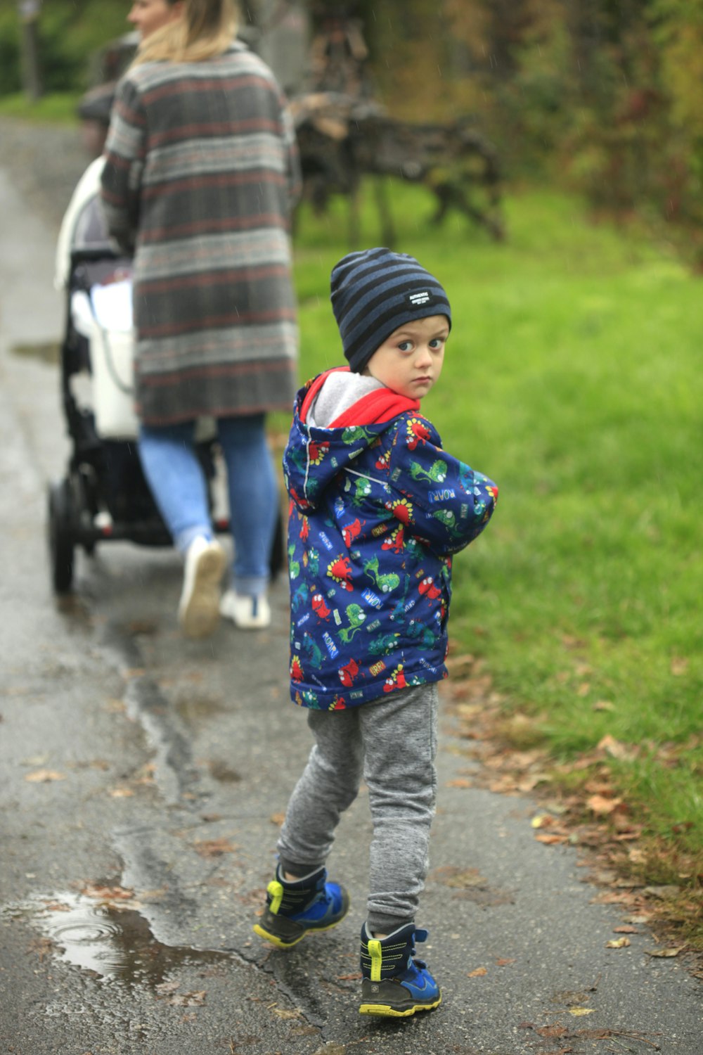 child in blue and red jacket and gray pants walking on gray concrete pathway during daytime