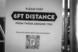 A black and white sign instructs people to maintain a distance of 6 feet from those around them. There is a QR code at the bottom for accessing a full menu with a directive to point a camera at it.