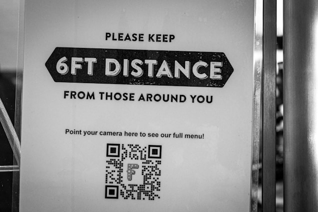 A black and white sign instructs people to maintain a distance of 6 feet from those around them. There is a QR code at the bottom for accessing a full menu with a directive to point a camera at it.