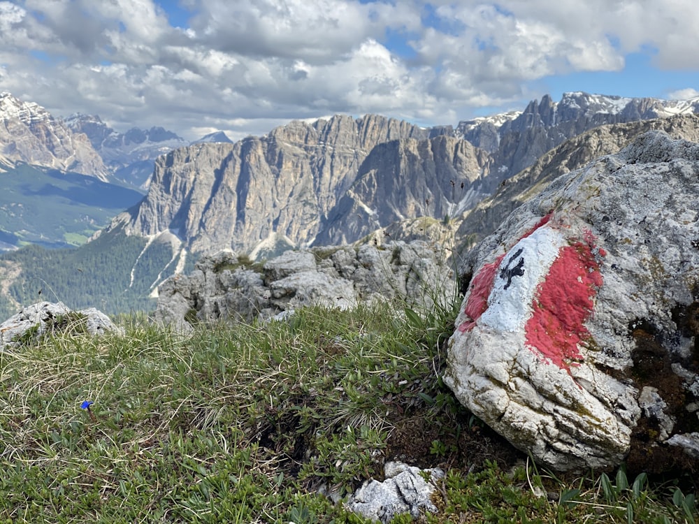 gray and red rock on green grass field near gray rocky mountain under white cloudy sky