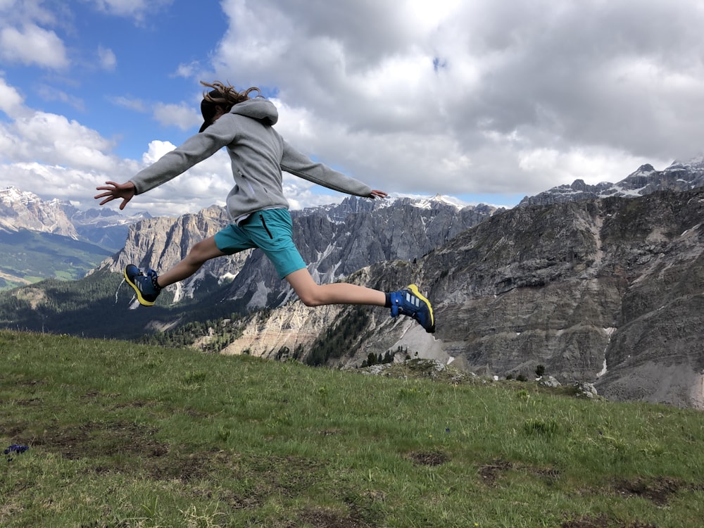 man in gray hoodie and blue denim jeans jumping on green grass field during daytime