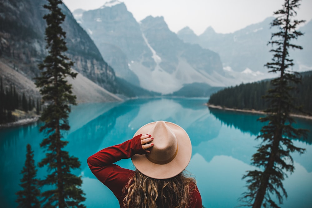 茶色の日よけ帽と赤い長袖シャツを着た女性が湖の近くの岩の上に座っている