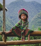 woman in green and red long sleeve dress sitting on brown wooden swing during daytime