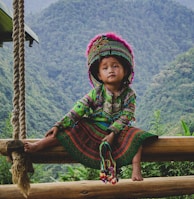 woman in green and red long sleeve dress sitting on brown wooden swing during daytime