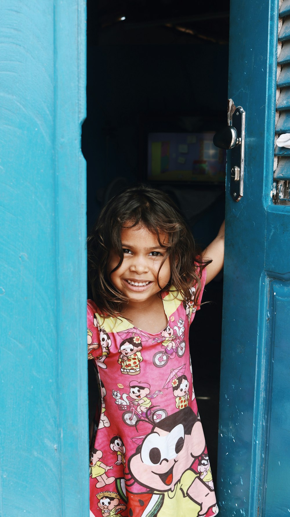 girl in pink and white hello kitty shirt standing beside blue wooden door