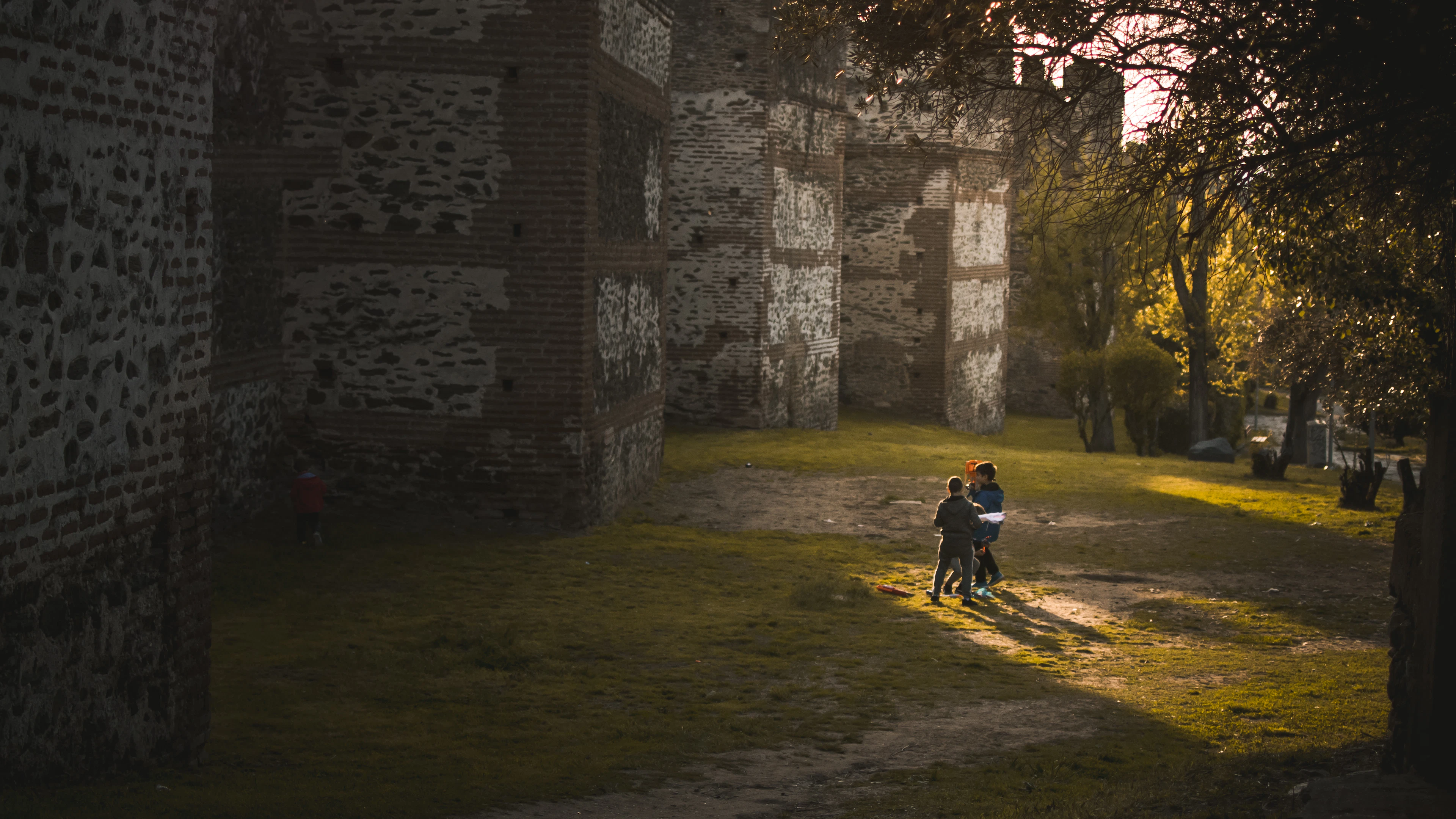 Evening sun raking across the Byzantine walls of Thessaloniki's Upper Town, children running along the grass at the foot of the tall banded ramparts.