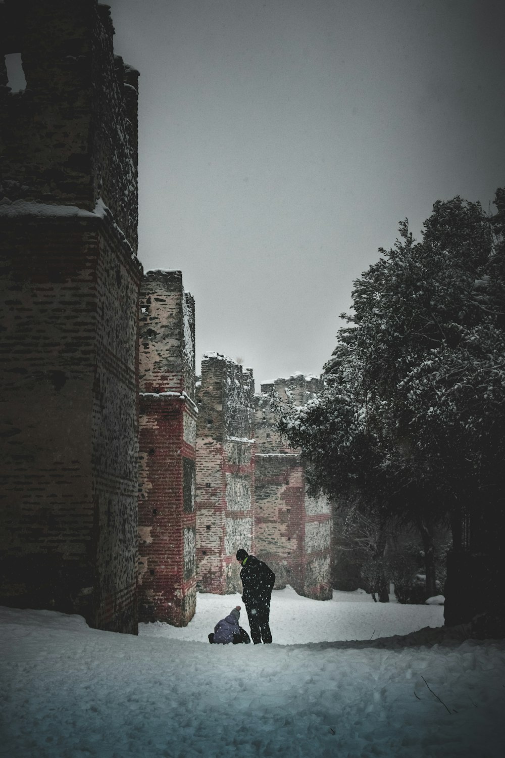 person in black jacket walking on snow covered ground near brown brick building during daytime