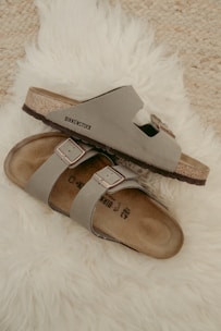 Soft beige sandals with subtle gold buckles placed on a smooth ivory marble surface.