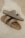 Two beige Birkenstock sandals are placed casually on a fluffy white rug. The sandals have a simple, comfortable design with leather straps and metallic buckles.