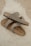 Two beige Birkenstock sandals are placed casually on a fluffy white rug. The sandals have a simple, comfortable design with leather straps and metallic buckles.