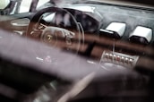 A luxury car interior showcases a sleek steering wheel with a prominent logo, surrounded by high-end materials and advanced controls. The dashboard features modern design elements and metallic accents, emphasizing a sense of sophistication and speed.