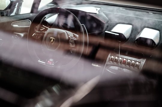 A luxury car interior showcases a sleek steering wheel with a prominent logo, surrounded by high-end materials and advanced controls. The dashboard features modern design elements and metallic accents, emphasizing a sense of sophistication and speed.