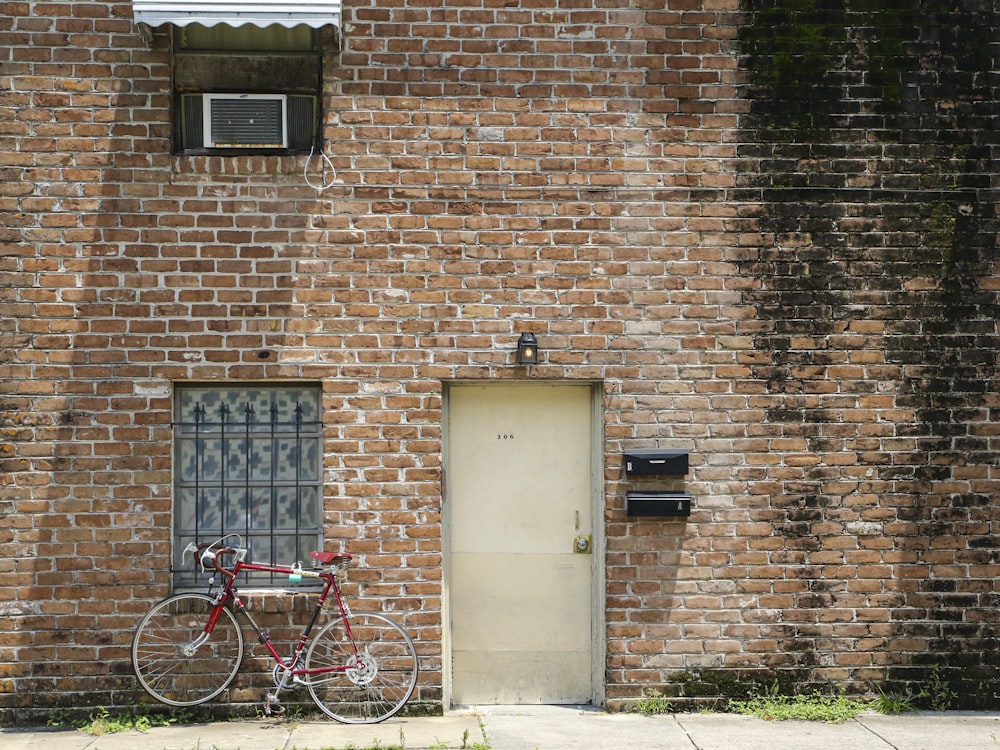red bicycle parked beside brown brick wall