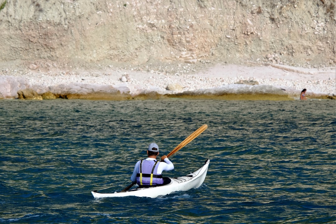 man in red and white vest riding on white kayak on body of water during daytime