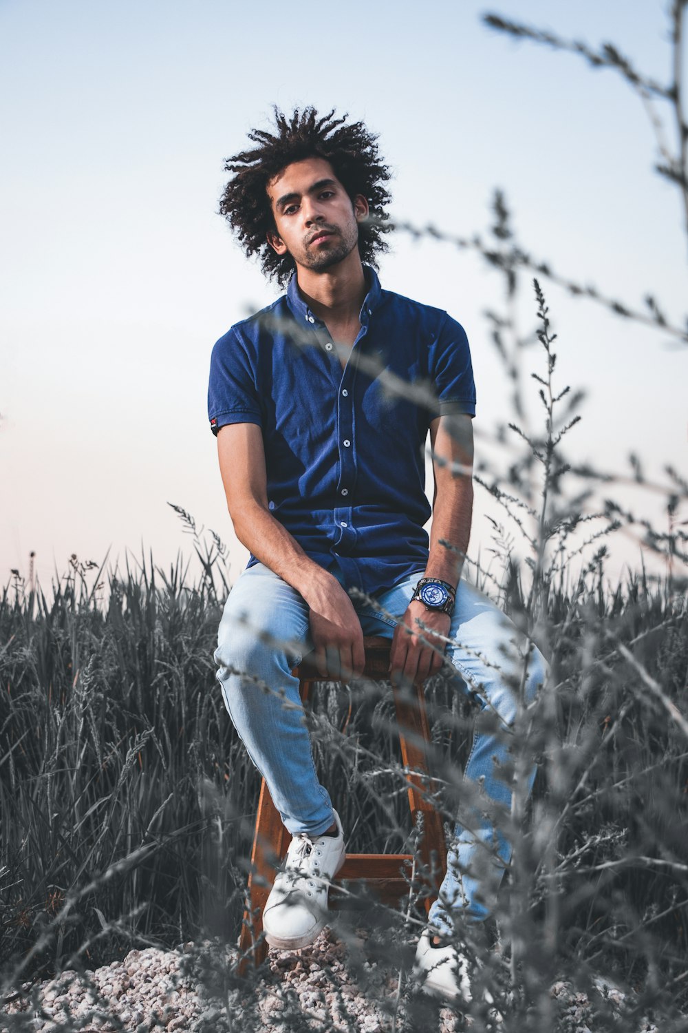 man in blue polo shirt and blue denim jeans sitting on brown grass during daytime