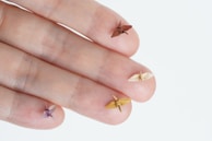Five tiny origami cranes rest delicately on the tips of human fingers, showcasing intricate paper folding on a small scale.