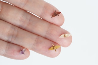Five tiny origami cranes rest delicately on the tips of human fingers, showcasing intricate paper folding on a small scale.