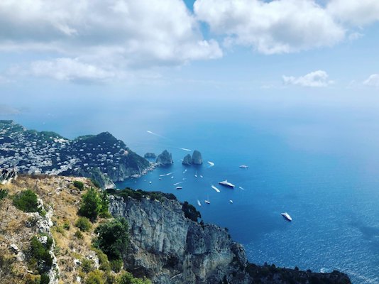Green and brown mountain beside body of water under white clouds and blue sky during daytime — Capri, Italy