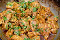 Close-up of sizzling tandoori chicken with charred edges and vibrant spices.