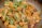 A close-up of cooked chicken pieces garnished with fresh green herbs and sliced green chilies, served in a pan. The chicken appears to be seasoned with spices, giving it a rich, savory look.