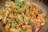 A close-up of cooked chicken pieces garnished with fresh green herbs and sliced green chilies, served in a pan. The chicken appears to be seasoned with spices, giving it a rich, savory look.