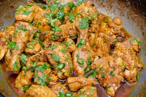 Close-up of a sizzling spicy chicken dish garnished with fresh herbs on a rustic plate.