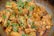A close-up of cooked chicken pieces garnished with fresh green herbs and sliced green chilies, served in a pan. The chicken appears to be seasoned with spices, giving it a rich, savory look.