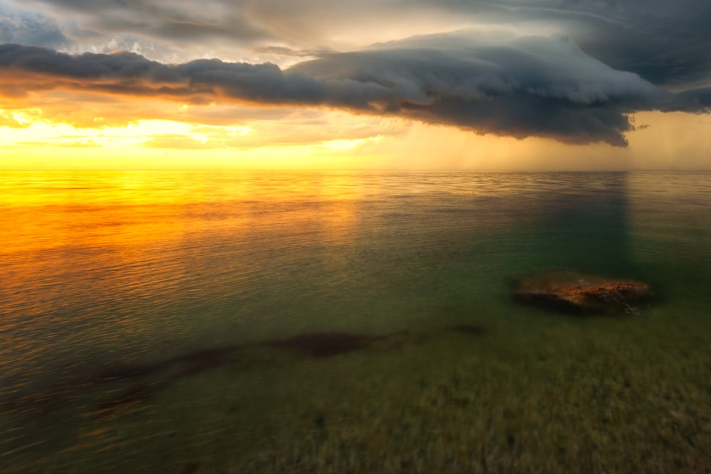 body of water under cloudy sky during sunset