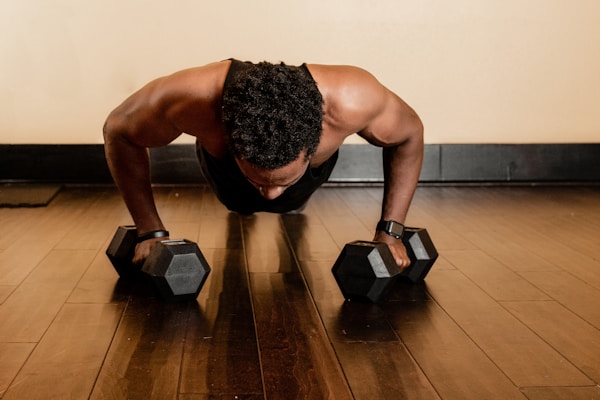 man in black tank top and black shorts holding black dumbbells