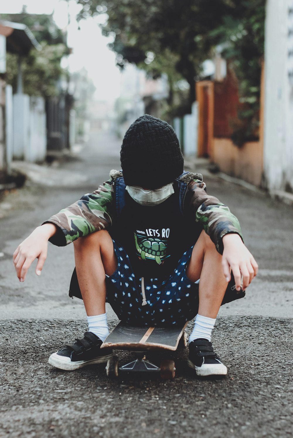 child in black and green shirt and black pants wearing black knit cap sitting on concrete