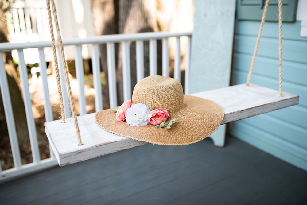 a straw hat with flowers on a porch swing