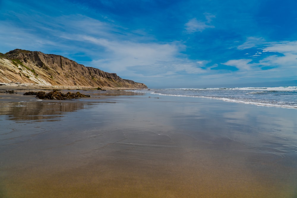 brown rocky mountain beside sea under blue sky during daytime