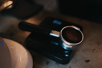 A barista carefully measuring freshly roasted coffee grounds into a scale on a black countertop.