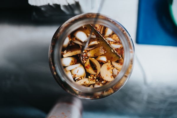 A top-down view of a glass jar filled with sliced vegetables and spices, likely pickles, with a liquid brine.