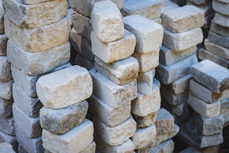 Multiple stacks of rectangular stone bricks arranged in an organized manner. The bricks have a variety of beige, gray, and white hues and some exhibit signs of wear and slight weathering.