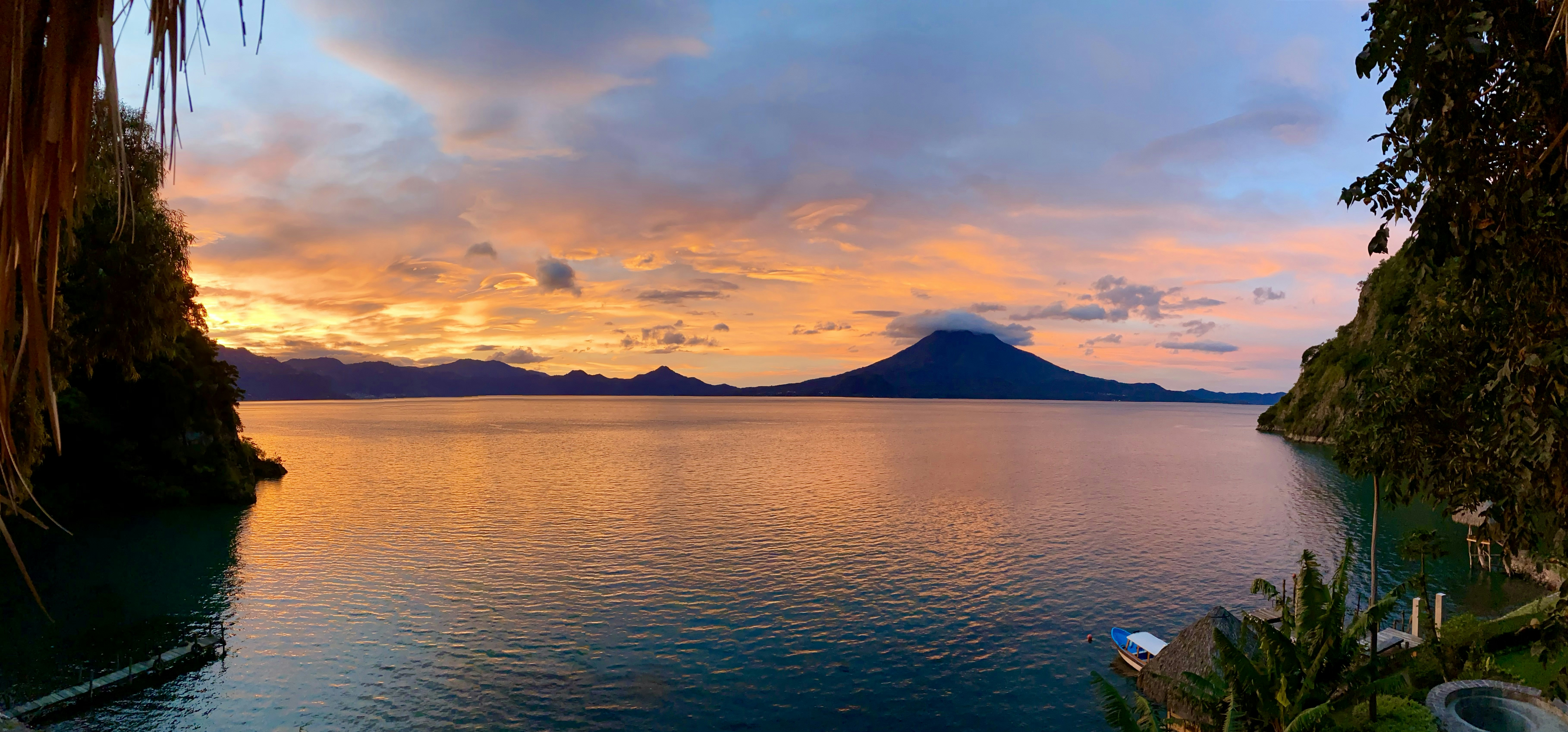 A serene view of Arenal Volcano framed by lush rainforest under a vibrant sunset sky.