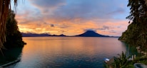 A scenic view of Lago de Coatepeque with tourists dining nearby at sunset.