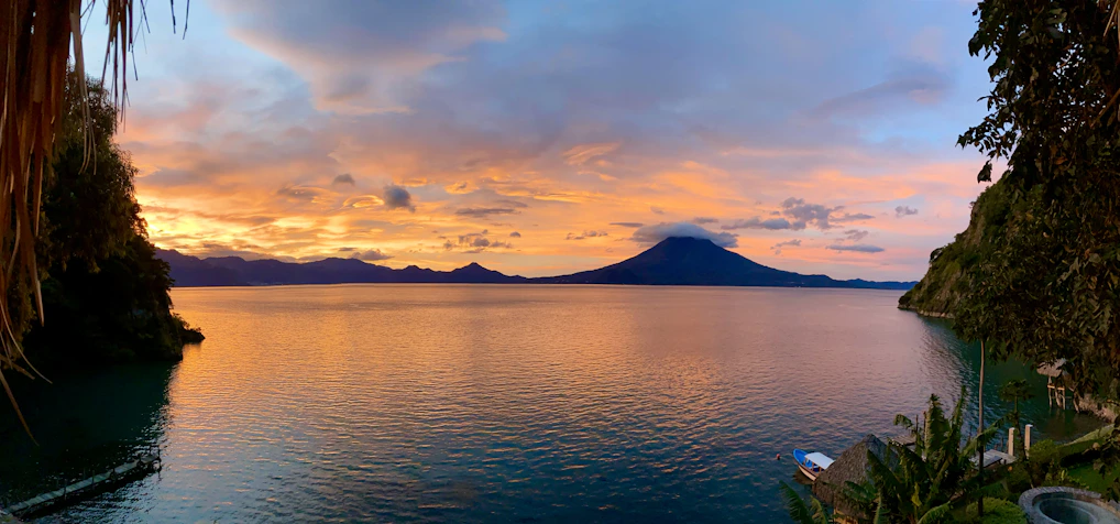 A vibrant sunset over the Arenal Volcano with lush greenery in the foreground.