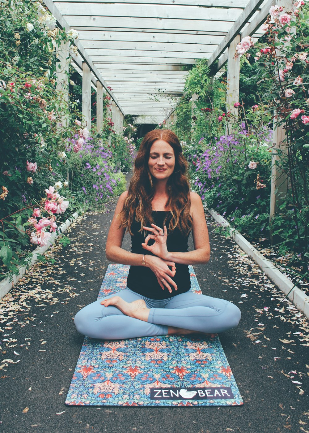 woman in black tank top and blue denim jeans sitting on blue mat surrounded by flowers