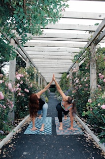 2 women in blue tank top and black leggings standing near pink flowers during daytime