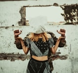 A woman with a white cloth covering her head stands in front of a man whose hands are bound behind her back. They are positioned against a rough, textured wall with an opening, creating a sense of entrapment or confinement.