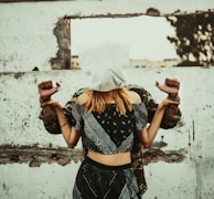 A woman with a white cloth covering her head stands in front of a man whose hands are bound behind her back. They are positioned against a rough, textured wall with an opening, creating a sense of entrapment or confinement.